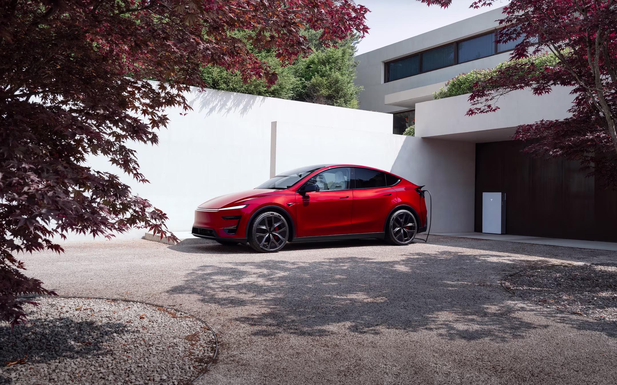 Ultra Red Model Y charging with a Wall Connector in front of a residential garage