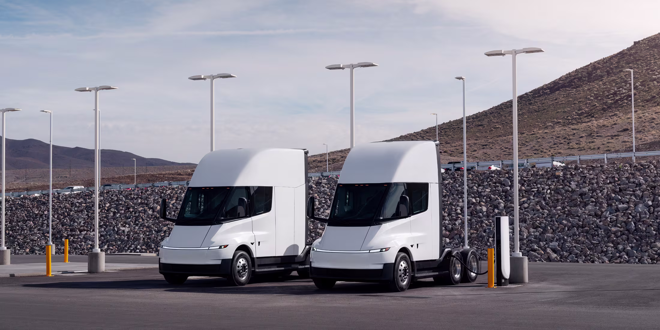 Two electric Semi trucks charging side-by-side at Semi chargers by the highway