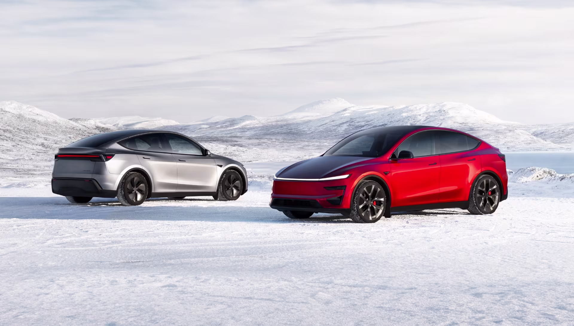 Red and quicksilver Model Y vehicles parked on a snowy plain in front of snow-covered mountains
